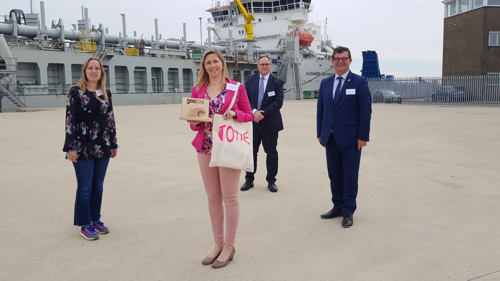 Foto van prijsuitreiking SeaZone project met Liesbet, de Burgemeester Bart Tommelein en meer met op de achtergrond een boot.